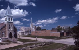 This Charles Herman photo of the Holy Family Catholic Church, St John Lutheran Church and St. John Lutheran School in Alma features Herman's trademark blue skies and puffy white clouds.